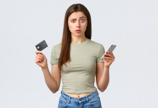 Online shopping, home lifestyle and people concept. Confused and puzzled pretty woman with credit card and mobile phone raise one eyebrow and looking camera uncertain, white background.