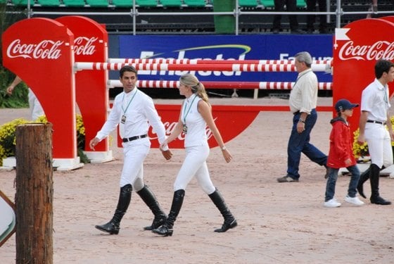 Athina e Doda Miranda caminham na pista de competição do Athina Onassis International Horse Show, onde aparece o obstáculo que a Rio de Janeiro Refrescos montou para o evento.