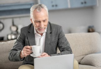 Mature businessman. Cheerful male person being at home and bowing head while staring at his laptop